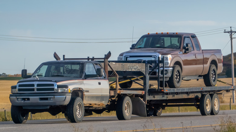 A Dodge Ram pickup truck towing a flatbed trailer with a brown Ford F-Series pickup truck securely fastened on top.