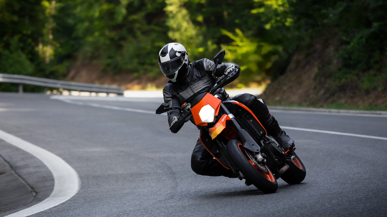 Motorcyclist Riding Orange Motorcycle on Curved Road Outdoors