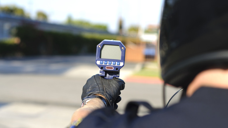 An over-the-shoulder shot of a cop holding a radar gun that is actually off at the roadway.