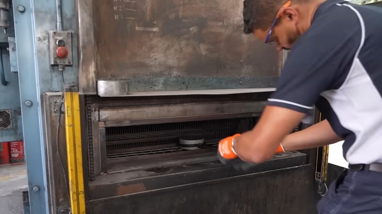 A man using tools to grab aluminum during the heating process prior to forging