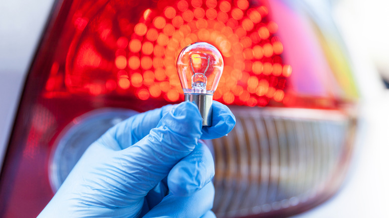 A gloved hand holding an incandescent brake light bulb against the taillight of a car