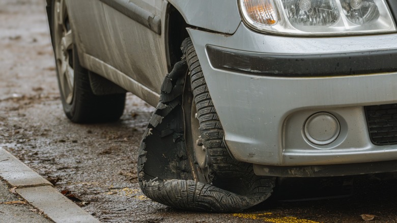 A car with a blown out tire by a sidewalk