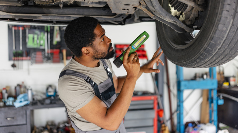 A mechanic holds a flashlight, inspecting the suspension on a car raised up on a shop jack
