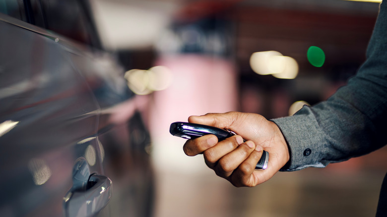 A man's hand holding a smart key fob near a car.