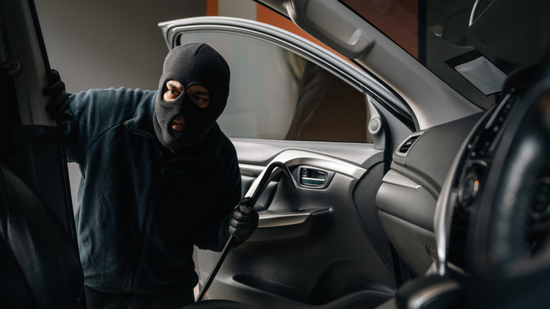 A thief in a black mask breaking into a car