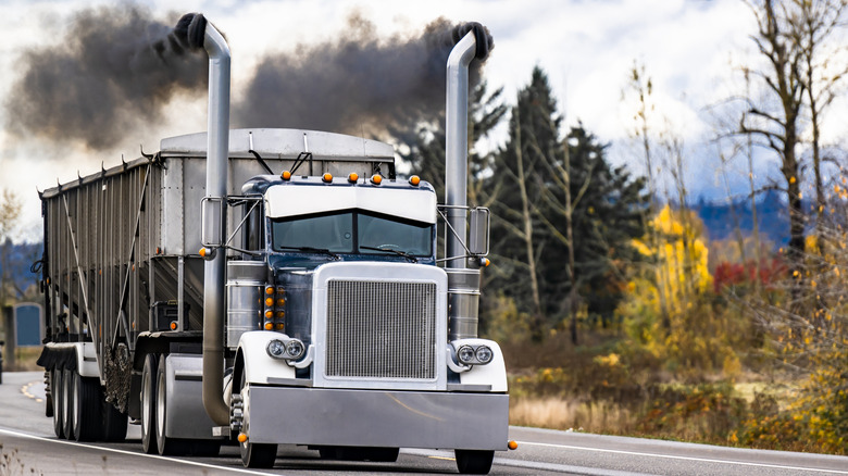 A vintage semi truck with black smoke billowing from its stacks
