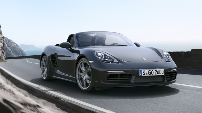 Front 3/4 of a topdown Porsche Boxster driven by a man in sunglasses.