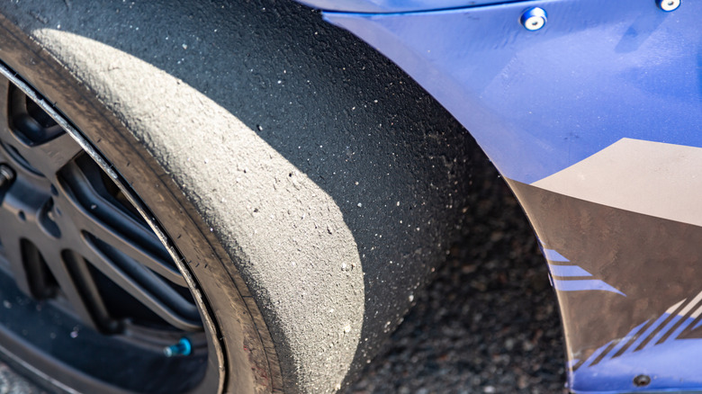A grippy slick tire at a track day or racing event beneath the fender of a car.