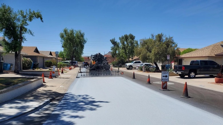 Rear view of a truck spraying a light gray reflective coating on a road in a residential Phoenix, Arizona neighborhood
