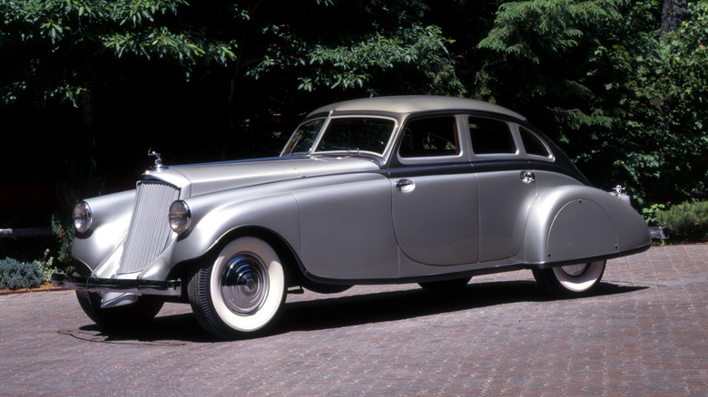 A Pierce-Arrow Silver Arrow sits parked on a cobblestone driveway in front of trees.