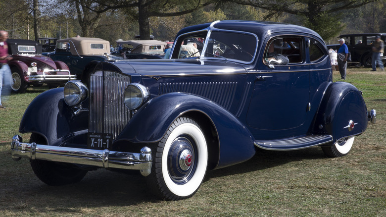 A blue Packard Twelve Model 1106 Sport Coupe sits parked on grass at a car show