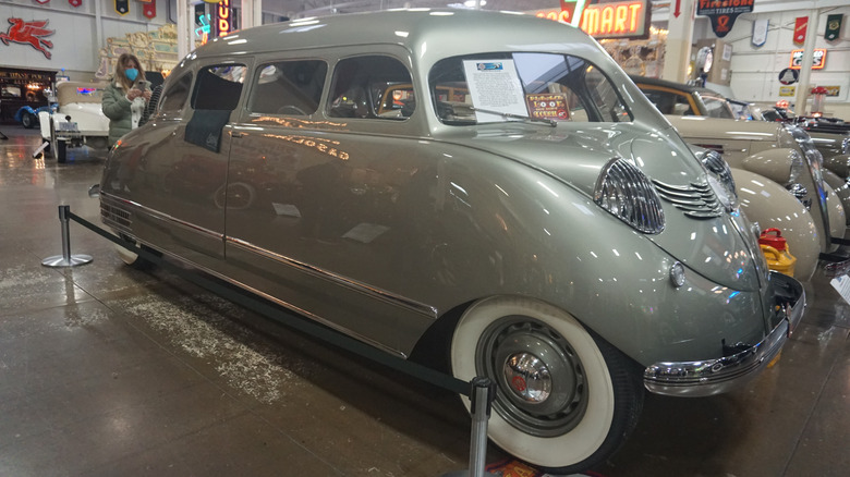 A gleaming silver Stout Scarab sits on exhibit under shining lights in an indoor vehicle museum.