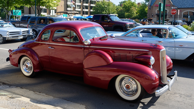 A red LaSalle Coupe sits in a public parking lot surrounded by other classic cars.