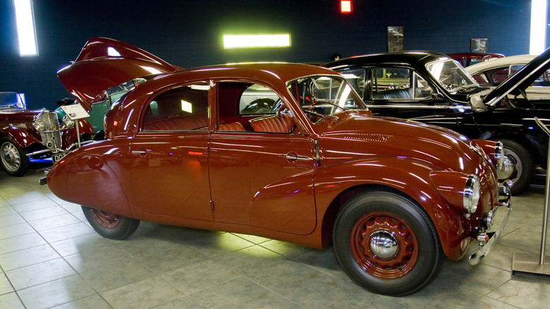 A red Tatra T97 sits parked with its trunk open under colored lights among other classics.