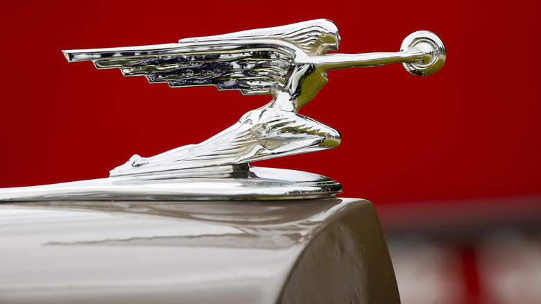 A hood ornament extends dramatically against a red background.