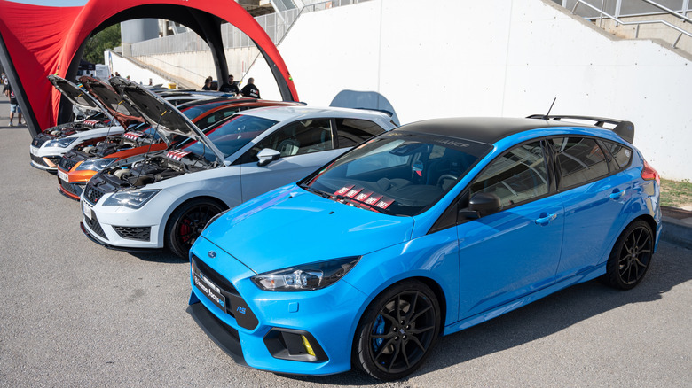 A blue Ford Focus RS displayed at a car meet, leading a lineup of hot hatches