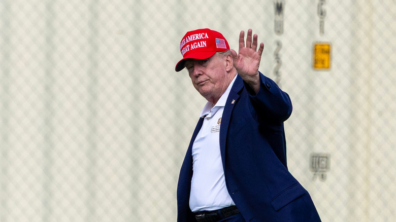 Donald Trump waves while walking in front of a chain link fence
