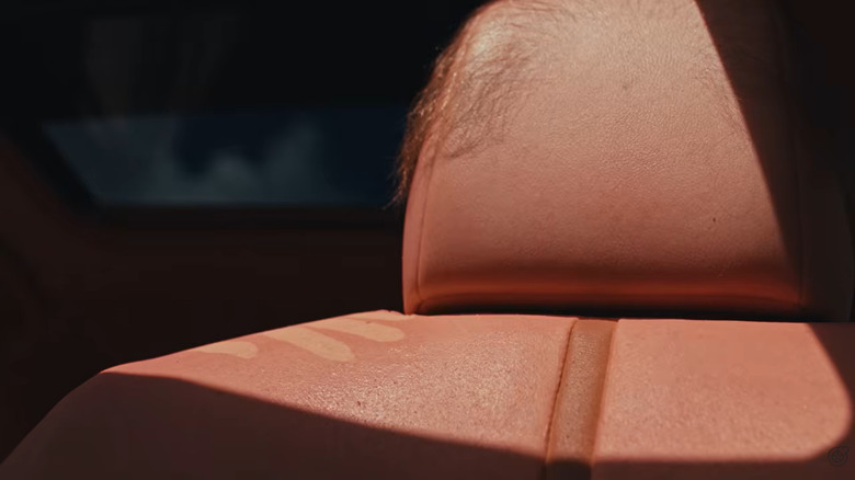 A close-up of a skin-upholstered front seat with some brown body hair on the head rest and a paler handprint showing how it responds to UV rays