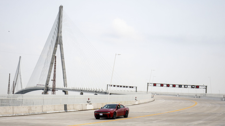 an electric dodge charger drives down an empty Gordie Howe International bridge on a cloudy day