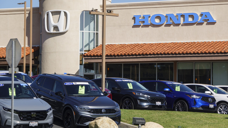 a honda car dealership in california. used vehicles from multiple automakers sit on the front lawn with green pricing tickets hanging from their rearview mirrors