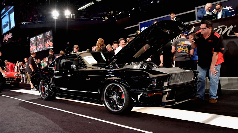 A black Ford Mustang coupe being showcased as the auction stand for the Barrett‑Jackson Collector Car Auction.