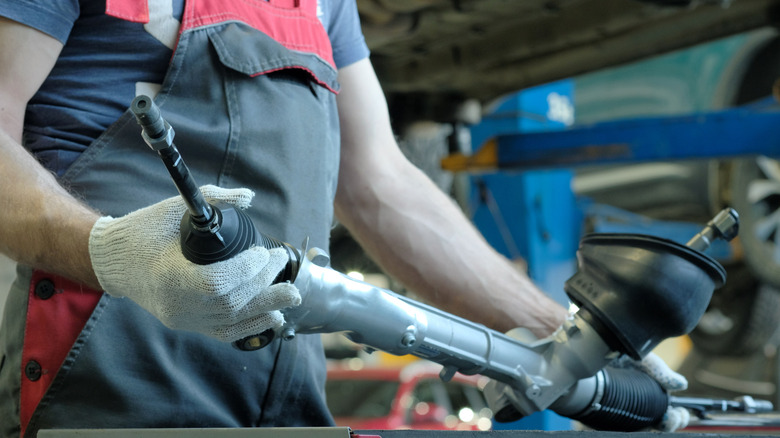 A mechanic holding a rack and pinion steering rack, tilting its right side.