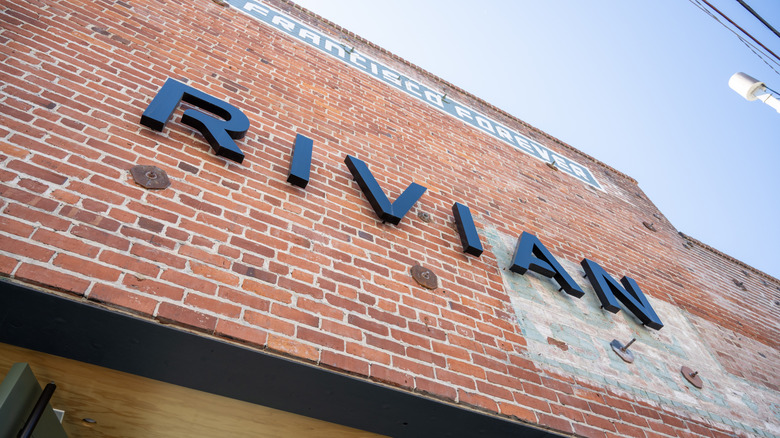 Brick destruction of Rivian storefront pinch achromatic 3D lettering against clear bluish sky, San Francisco, California, August 19, 2025.