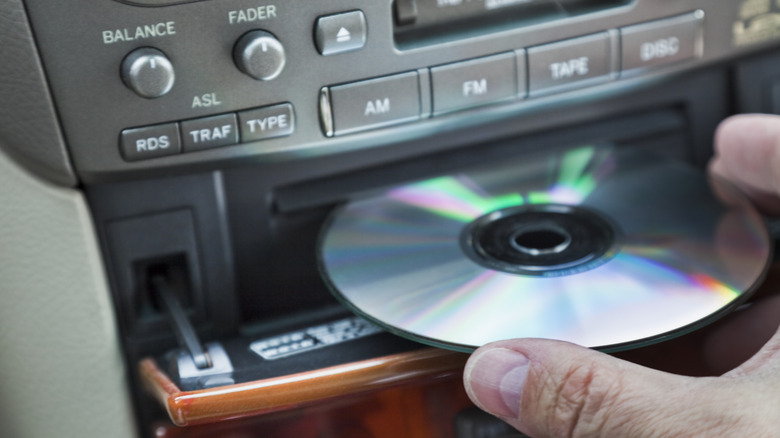 A hand inserting a CD into an in-car CD player