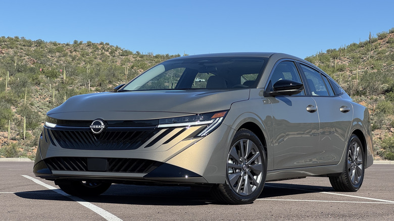 Front three quarters shot of a metallic tan Nissan Sentra SV parked in a lot in front of mountains covered in cactus and shrubs