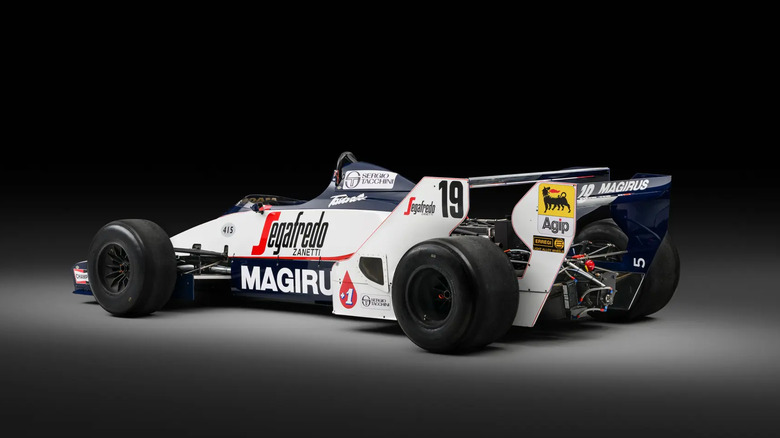 A rear three-quarters view of the Toleman TG183B-05 under a spotlight in a dark studio