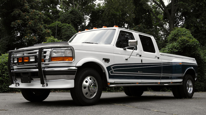 Front three quarters shot of a white and green F-350 Centurion Crew Cab Dually parked in front of green bushes