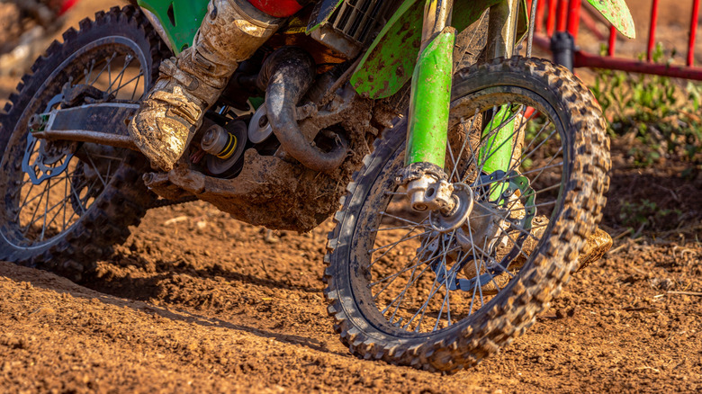 Dirty wheels, engine and boots on a muddy off-road motorcycle during an off-road race on a wet dirt track during a motocross endurance race.