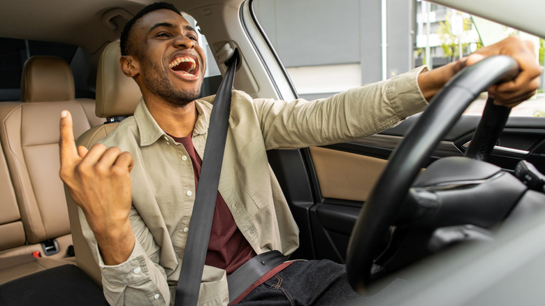 Joyful black man dancing in car, singing while driving his car. Road fun