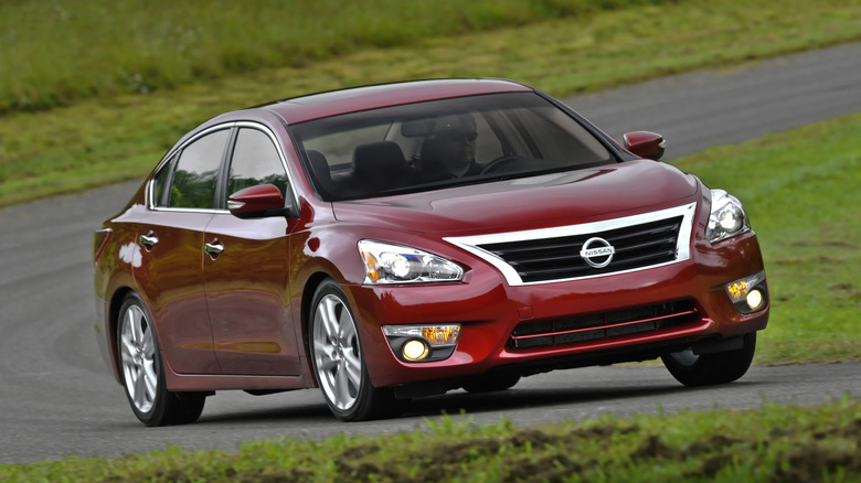 A red Nissan Altima drives on a winding road.