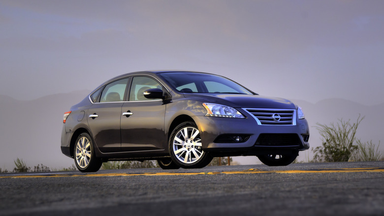 Side view of a blue 2013 Nissan Sentra parked on a desert road at sunset.