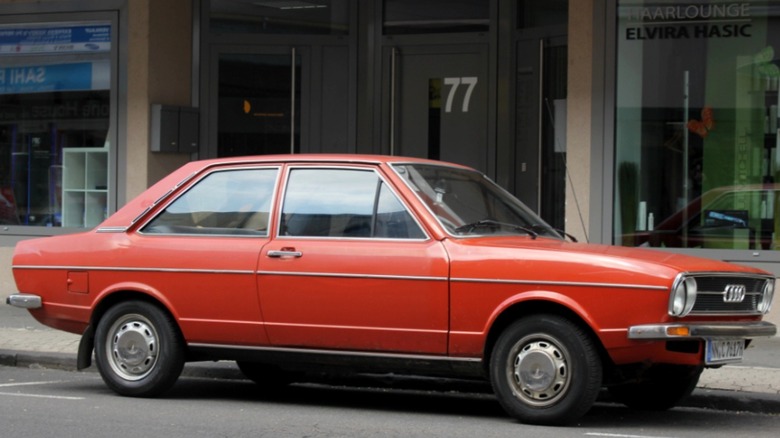 A red 1973 Audi 80/Fox parked in front of a store on a city street