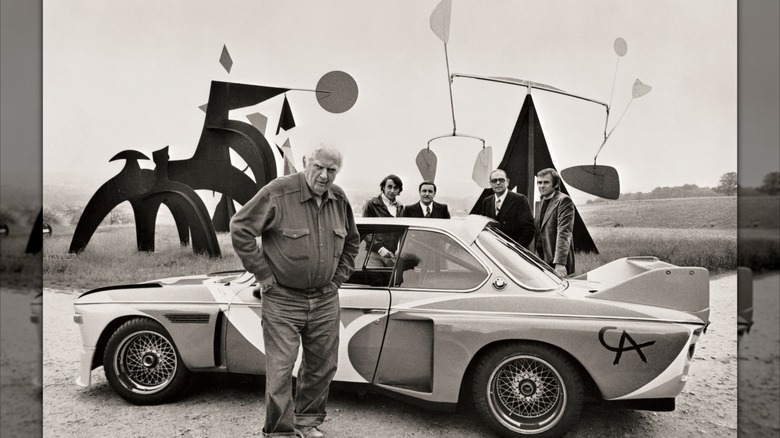 Sculptor Alexander Calder stands next to the 1975 BMW 3.0 CSL he painted, with a couple of his sculptures set in the background.