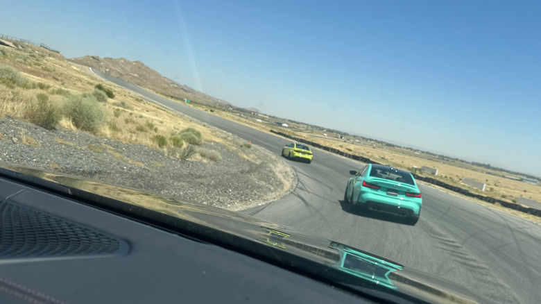 A photo of the rear of a turquoise M3 following a highlighter yellow one around a corner with lots of desert shrubs visible on the inside of the corner