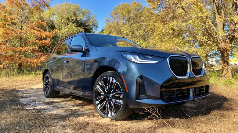 Front three quarters shot of a blue BMW X3 parked on dirt in front of colorful trees and blue skies