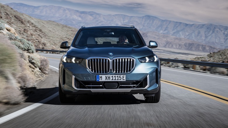 Front view of a 2024 BMW X5 driving around a curve on a desert road