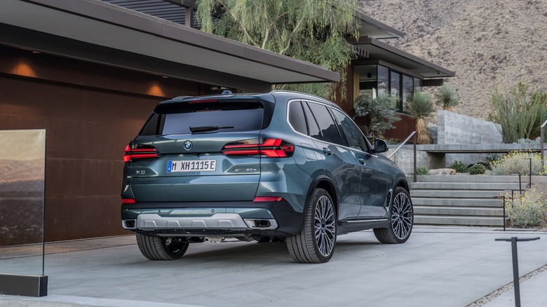 Rear 3/4 view of a 2024 BMW X5 parked in a driveway of a house in the desert