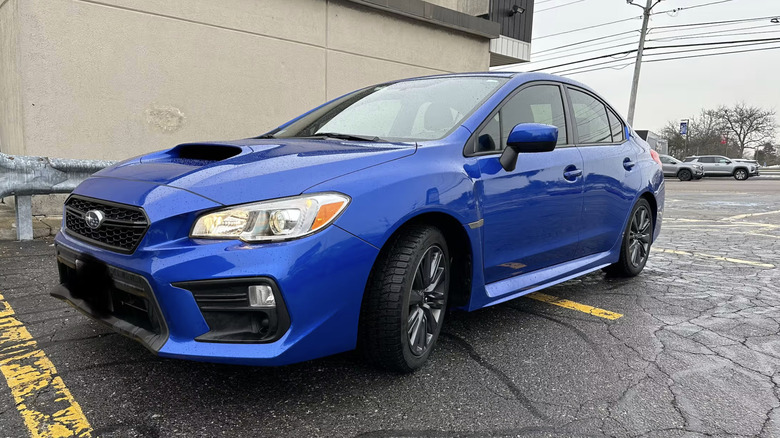 A blue Subaru WRX parked across two spaces on a cloudy day.