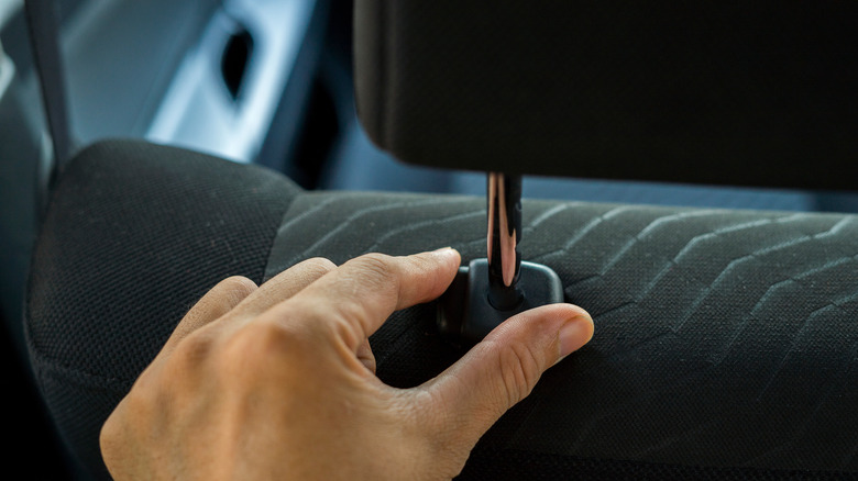 A hand on the adjustment tab of a car headrest.