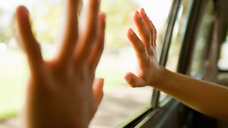 Two hands are pressed up against the inside of a car window.