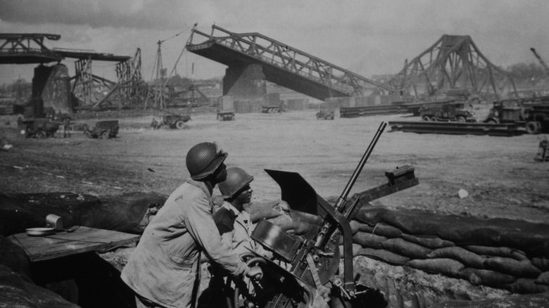 Two soldiers man a machine gun with the destroyed bridge that used to span the Rhine river, during World War II.