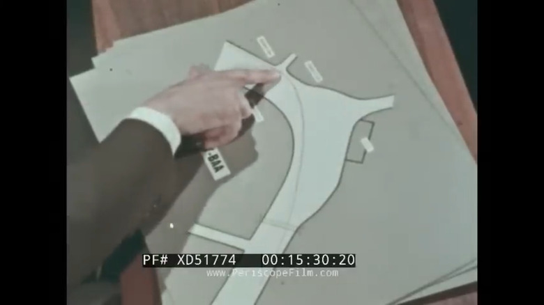 Geoff Duke's hand points at one of the Isle of Man TT course's corners as he guides his viewers through the proper line on a cardboard printed map.
