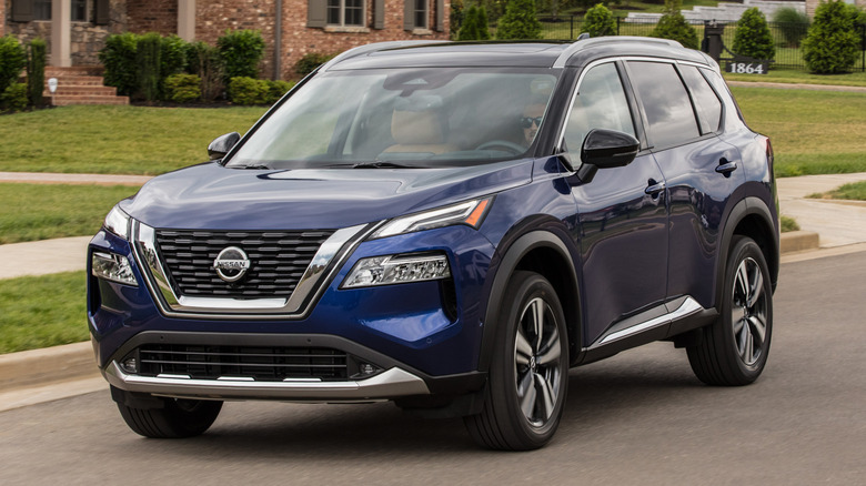 Blue 2021 Nissan Rogue driving along residential street with homes in the background.