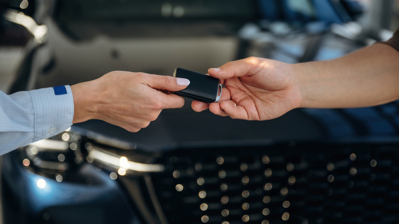 One person hands off a car key fob to another person in front of a new vehicle