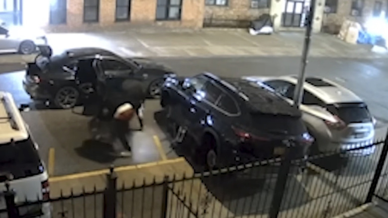 Alleged thieves removing wheels from a black SUV and moving them toward a waiting car