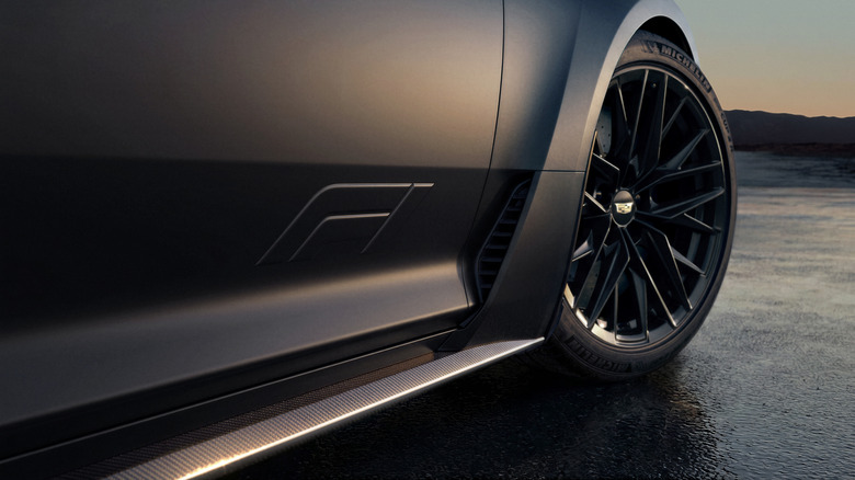 A close-up of the CT5-V Blackwing's front passenger door and front wheel showing the F1 logo and carbon bodykit in front of a dusky mountain sunset